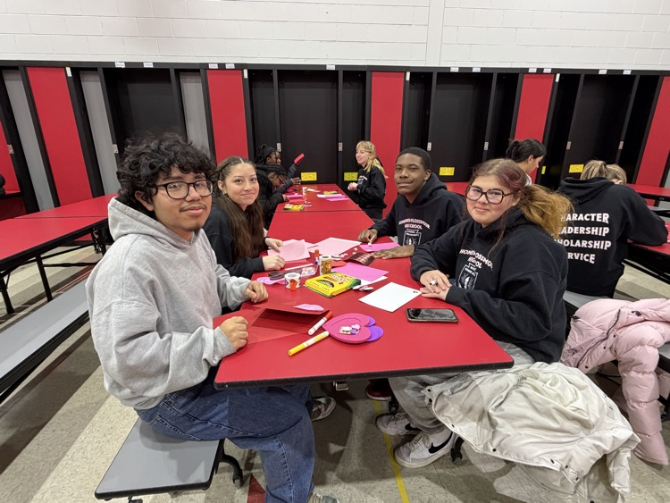 student sitting at a table working on a craft smiling at the camera