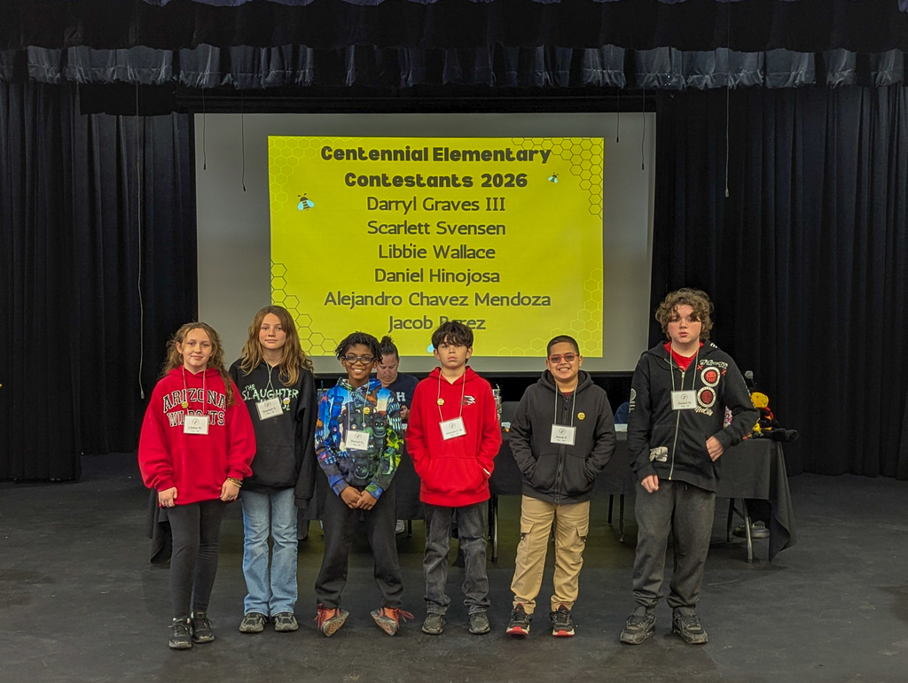 Centennial Elementary spelling bee contestants pose on stage in front of a screen displaying their names for the 2026 district competition.
