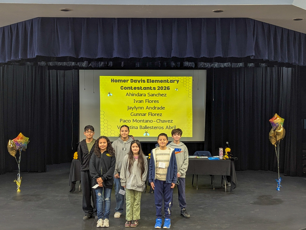 Homer Davis Elementary spelling bee contestants pose together on stage in front of a screen listing their names for the 2026 competition.