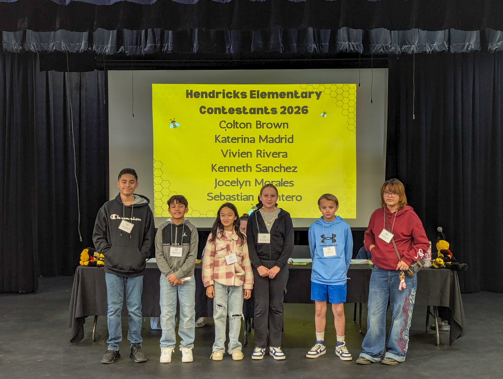Hendricks Elementary spelling bee contestants pose together on stage in front of a screen showing their names for the 2026 district spelling bee.
