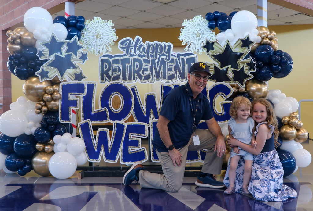 Retiree poses in front of 'Happy Retirement Flowing Wells' sign with two young children. 