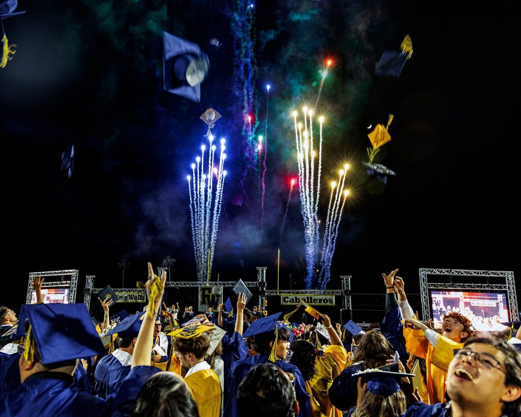 Flowing Wells High School graduates celebrate after commencement by tossing their caps into the air as colorful fireworks light up the night sky.