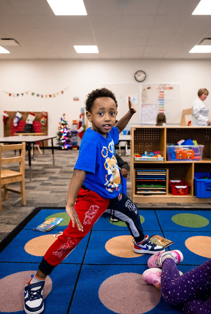 In a classroom, a young boy is playing Twister, showing concentration and energy amidst colorful decorations.