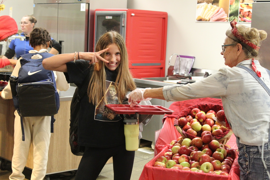 student posing for the camera as she receives an apple at lunch