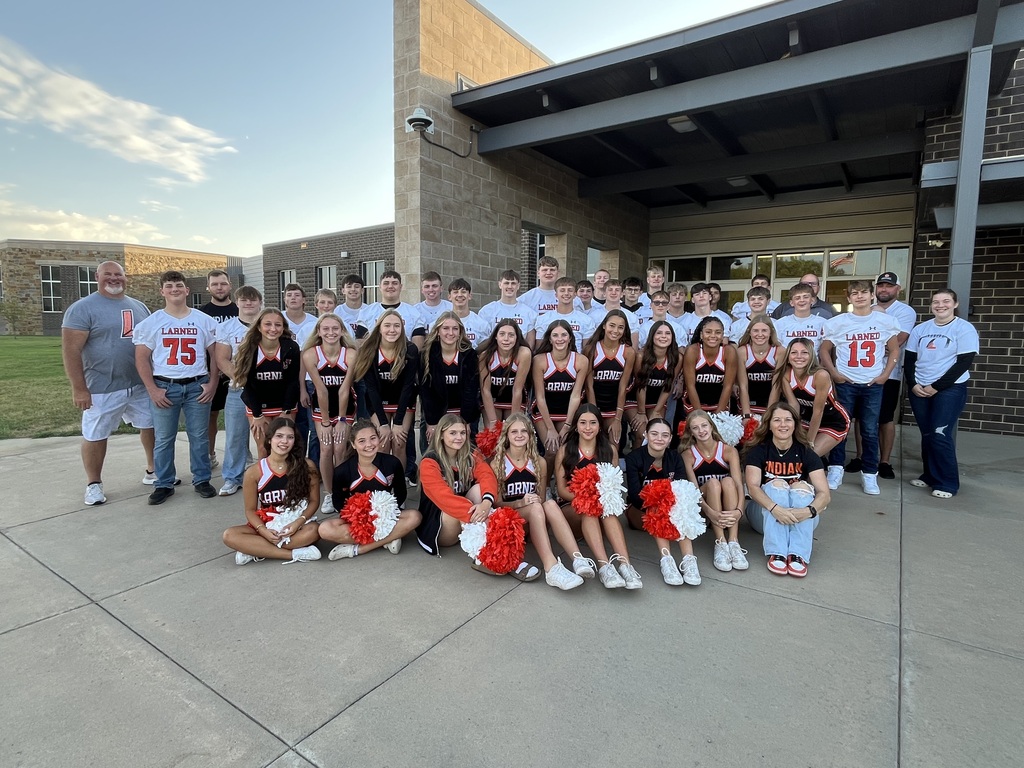 A cheerleading team poses for a photo in front of a brick-walled building with a metal roof.