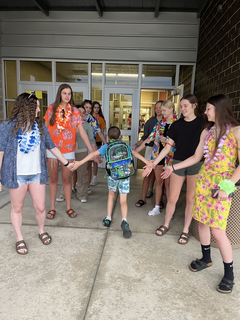A group of students, including a child, stand on a patio with their hands joined, wearing casual summer attire.