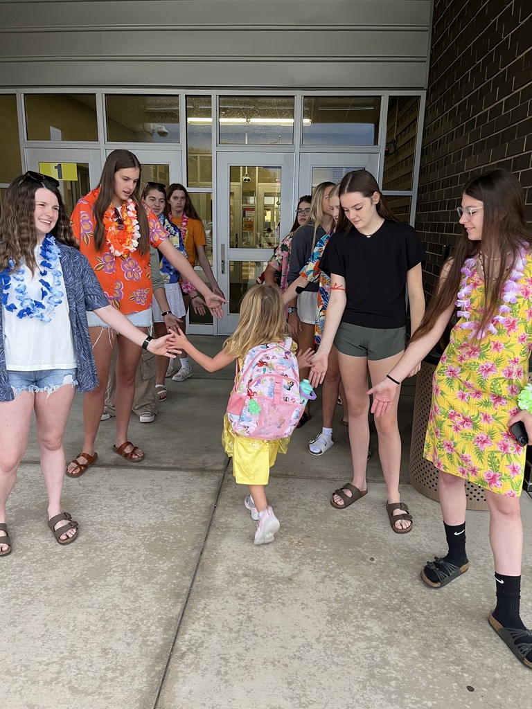 A group of young women hold hands with a young girl in front of a building.