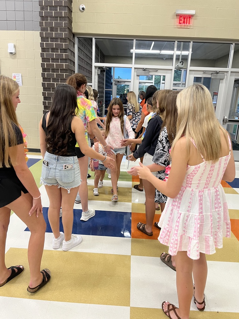 Group of girls standing in a hallway, holding hands. Bright light and checkered floor.