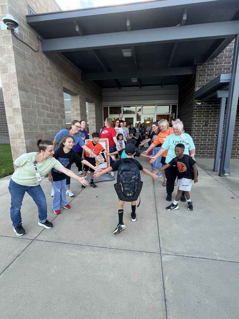 A group of people, including adults and children, stand outside a building, holding hands in a circle.
