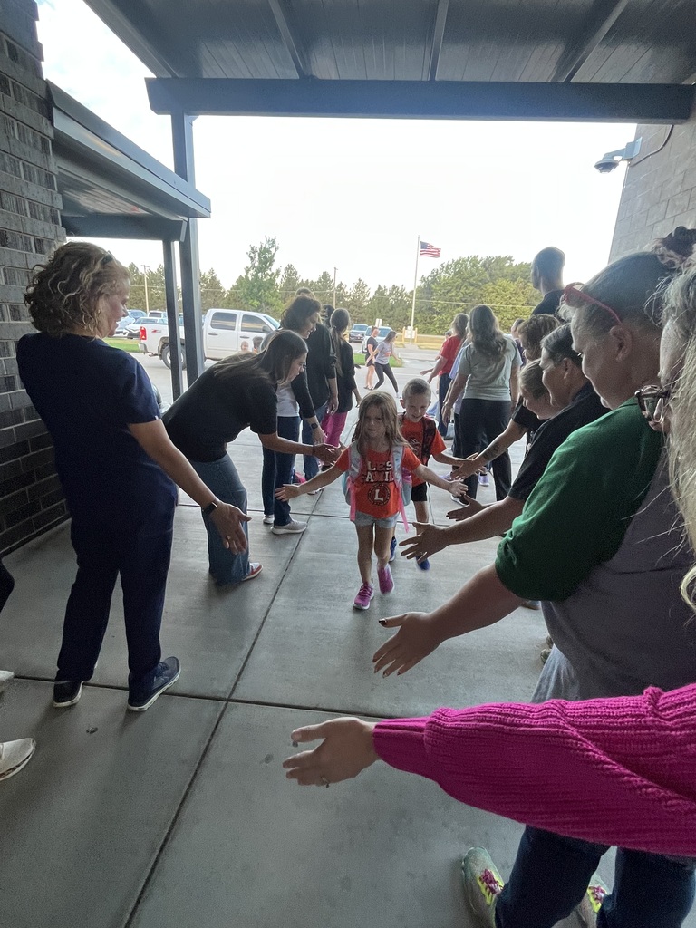 Group of adults in a school hallway, some holding hands, guiding a child in a bright shirt.