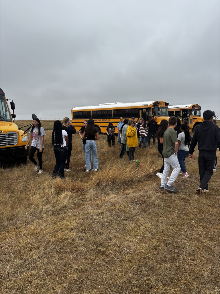 A group of people walks through a grassy field, with school buses parked in the background.