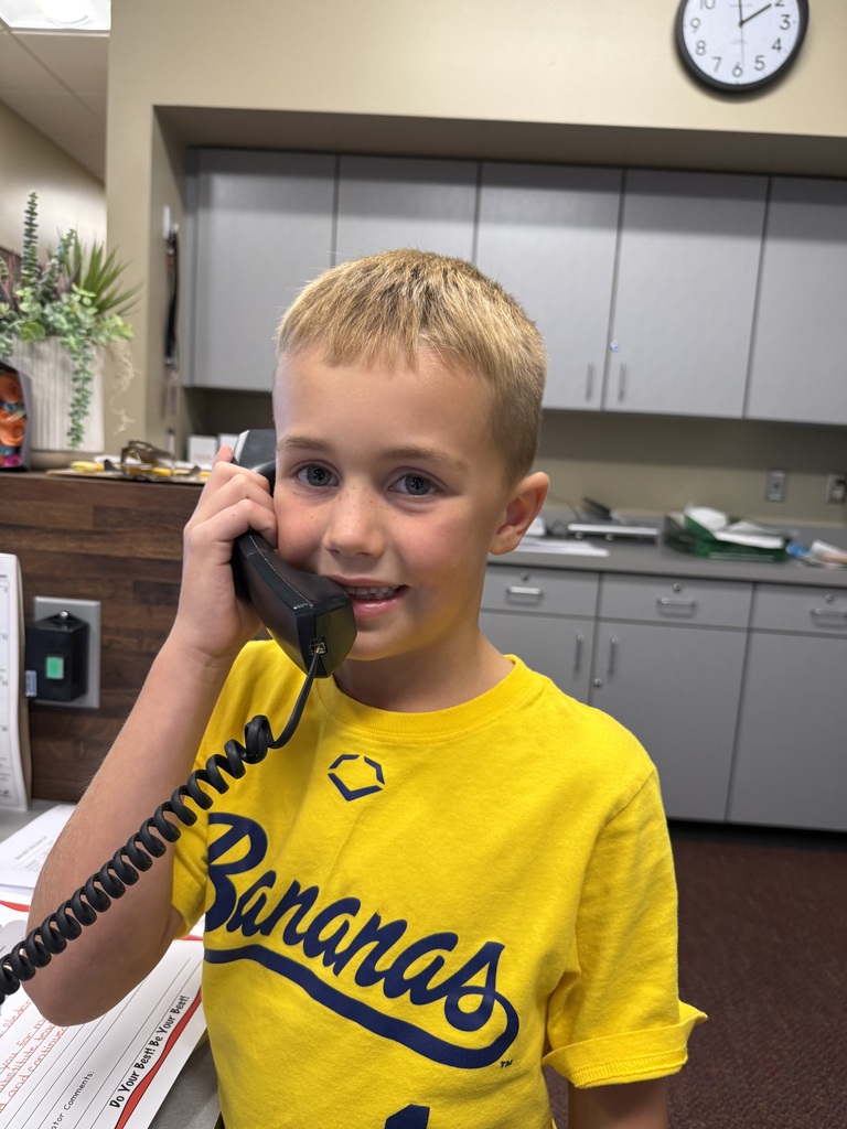 A young boy in a yellow t-shirt with "Bananas" printed on it, smiling and holding a phone.