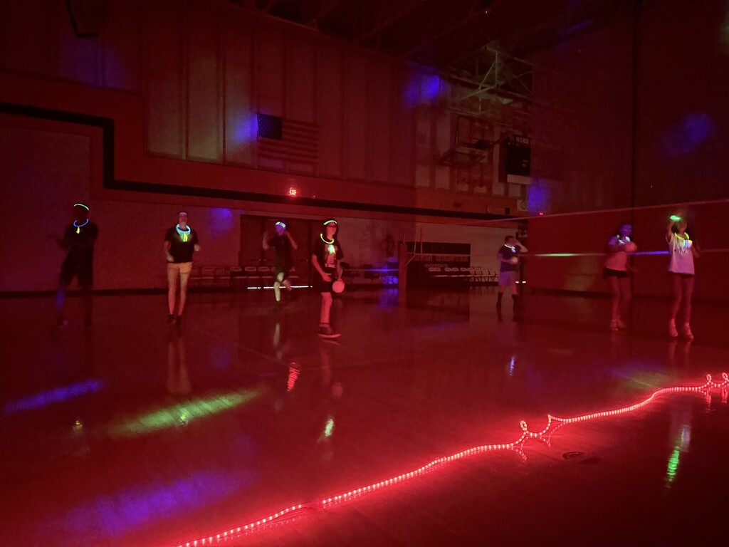 An indoor area with red and green lighting where people are playing laser tag. The floor reflects the lights.