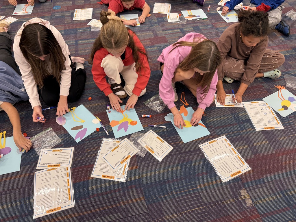 Children seated on floor, working on art projects with papers, scissors, glue, and other art supplies.