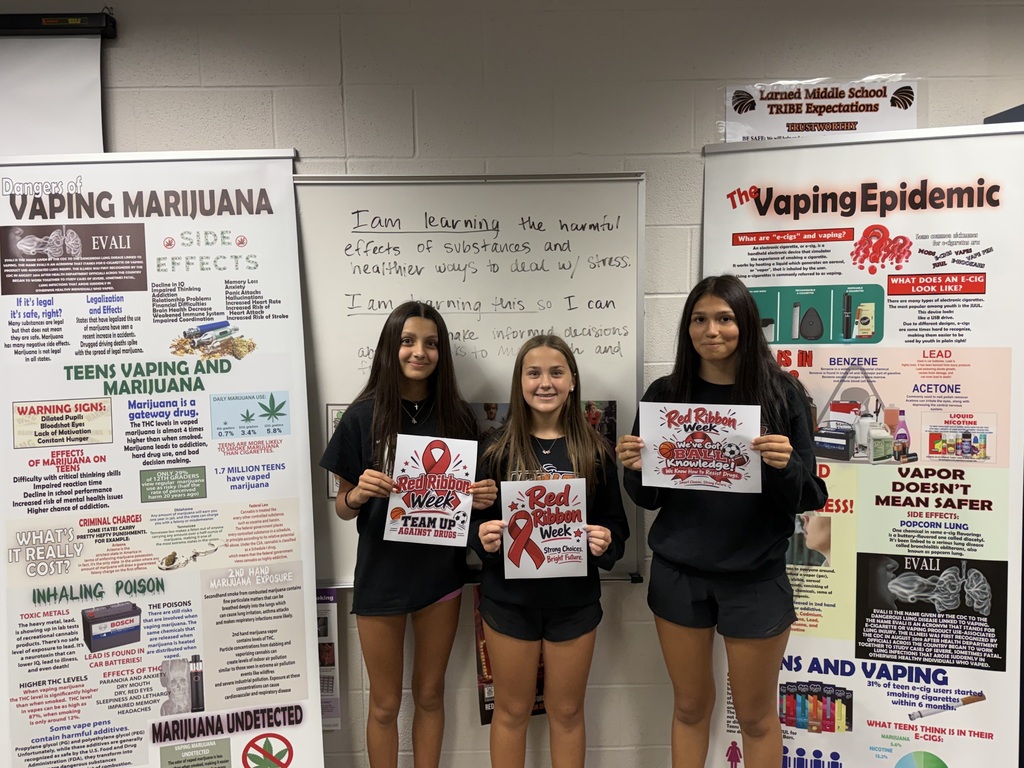 Four students stand in front of posters with health messages and graphics; they hold signs.