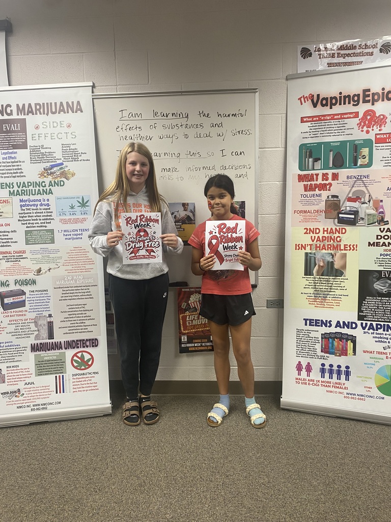 Two students standing next to each other, one holding a poster with a red ribbon.