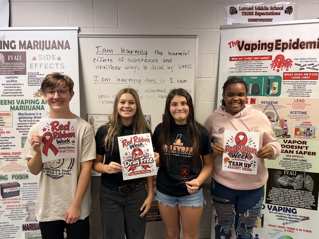 Five students stand in front of posters with health information, holding up signs with red ribbons.