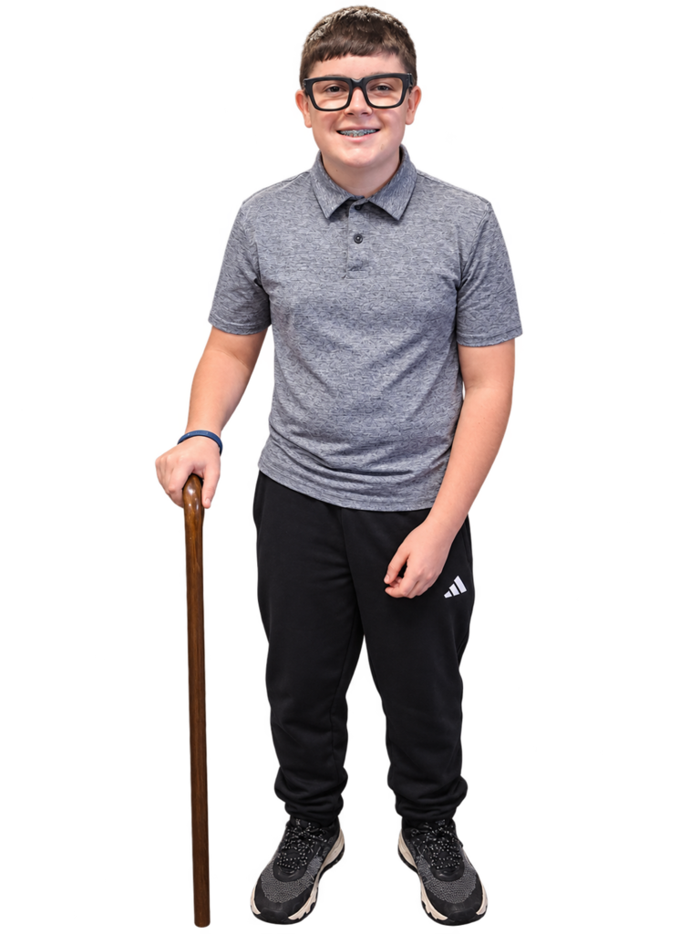 Person in glasses and gray polo shirt holding a wooden cane, smiling, standing against a black background.