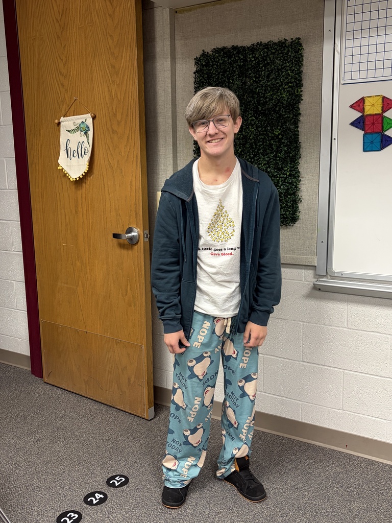 Boy in pajamas and jacket stands in hallway next to open door, smiling for photo.