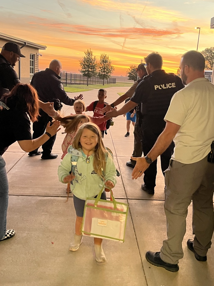 Adults, including police officers, help children walk in a line at sunset with bags in their hands.