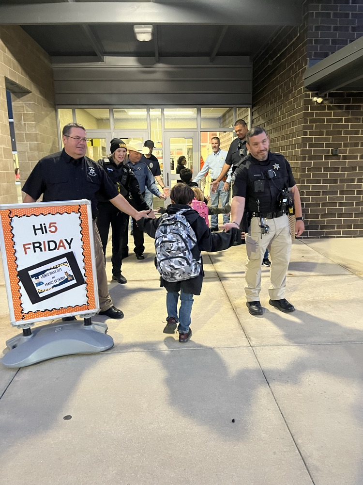 Officers help a young student with a backpack pass through a building entrance.