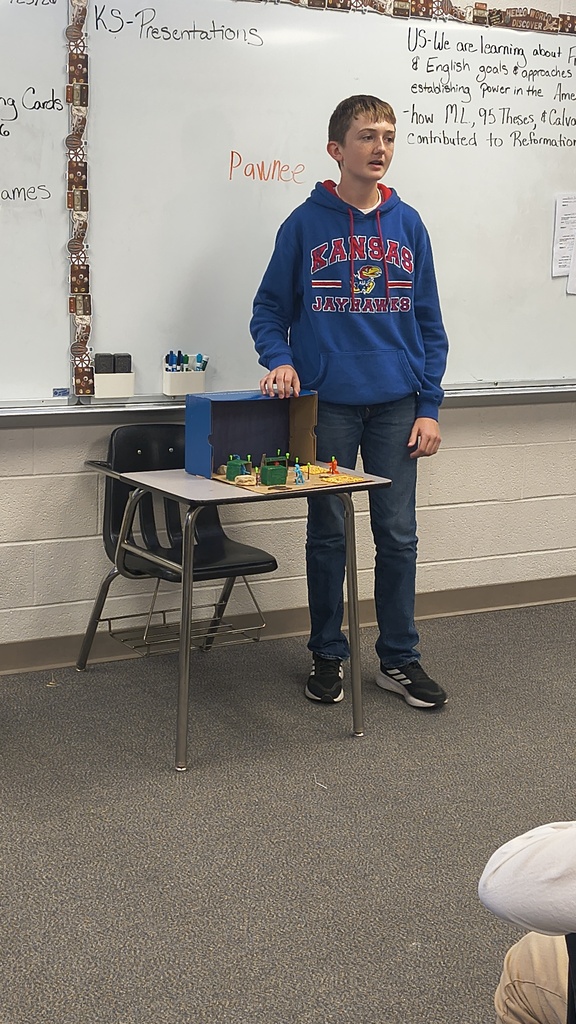 A student stands by a small table with a box and miniature items on top.