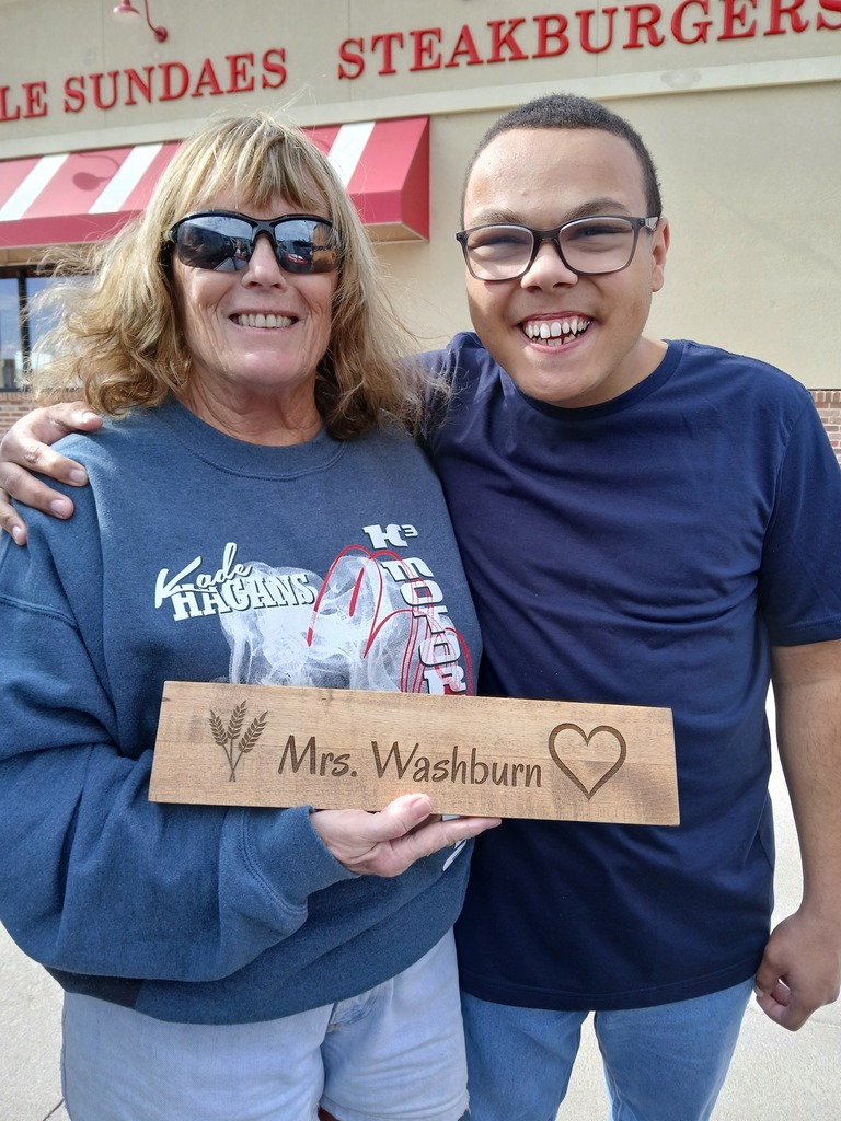 Adult and child hold sign with message for Mrs. Washburn, standing in front of restaurant.