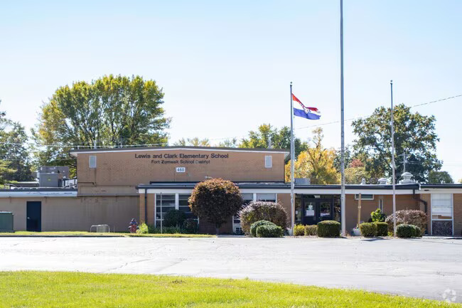 Lewis and Clark elementary - a brick building with two flag poles in front, with a varieyt of trees and plants all around