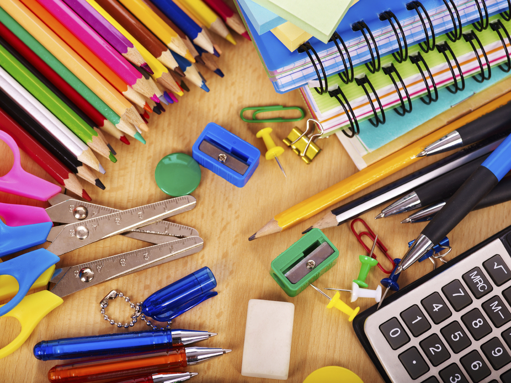 Various office supplies on a wooden desktop. Colored pencils, scissors, pens, notebooks, calculators, etc.
