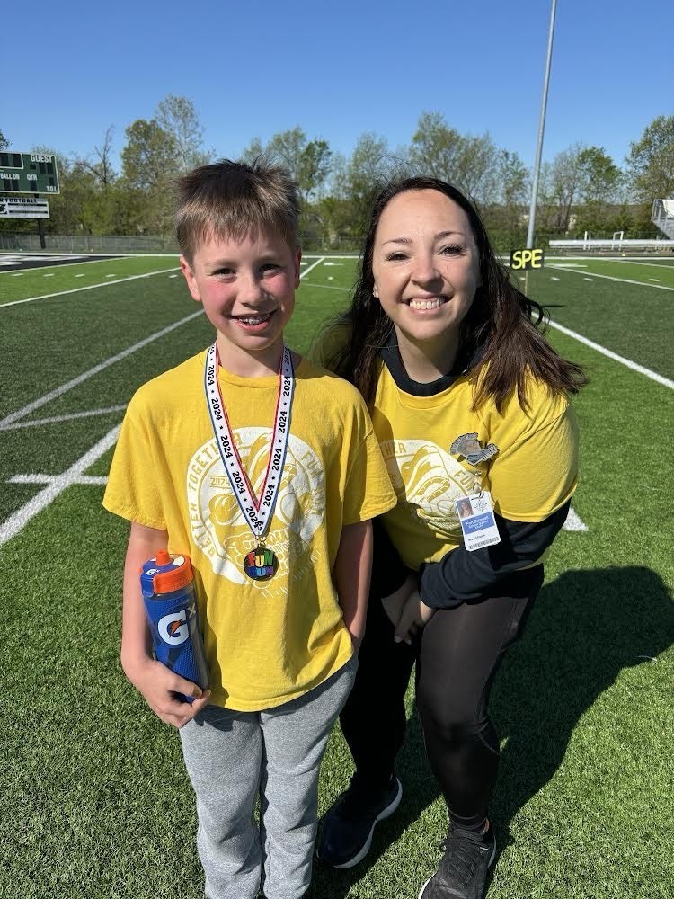 teacher and student kneeling, wearing yellow shirts, on a football field