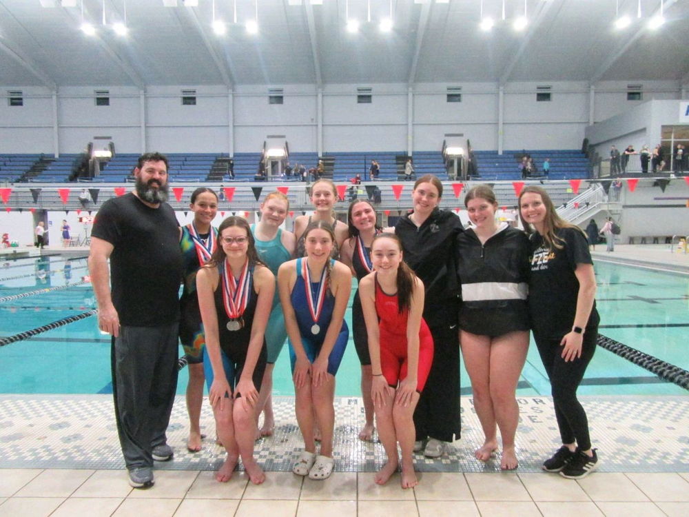 The girls swim team and coaches posing on the pool deck