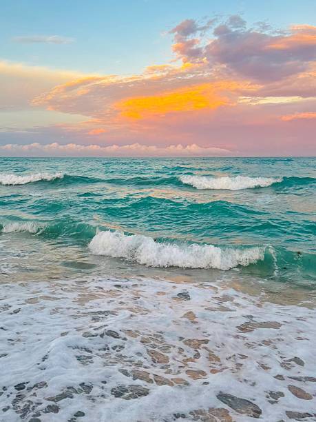 Waves breaking over a beach- cerulian blue with a orange and blue sky above