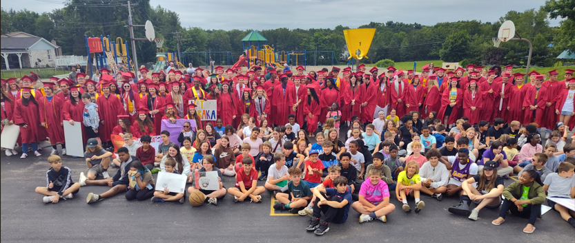 5th Graders sit in front of graduates in cap and gowns