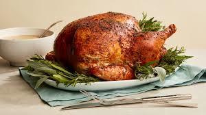 Roasted thanksgiving turkey on a plate, with greenery garnishes and a bowl of brown gravy
