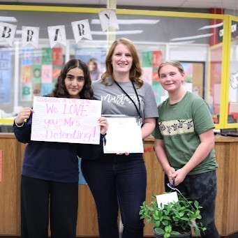Krystal Deterding, center, celebrates her announcement as FZSD educator of the year with two students, one holding a sign: We Love Mrs Deterding!