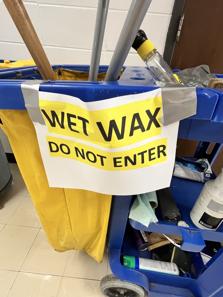 Paper sign reads WET WAX, DO NOT ENTER. Black font, highlighted in yellow. Taped to a blue and yellow custodial cart with brooms and other custodial equipment.