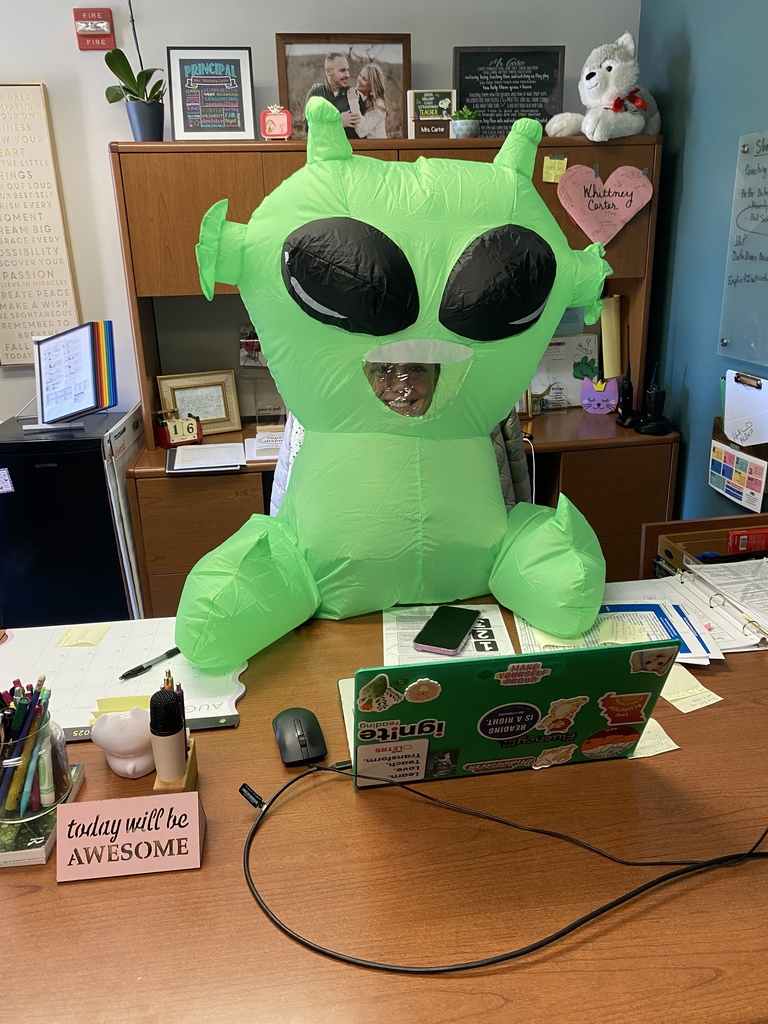 green alien sitting at desk