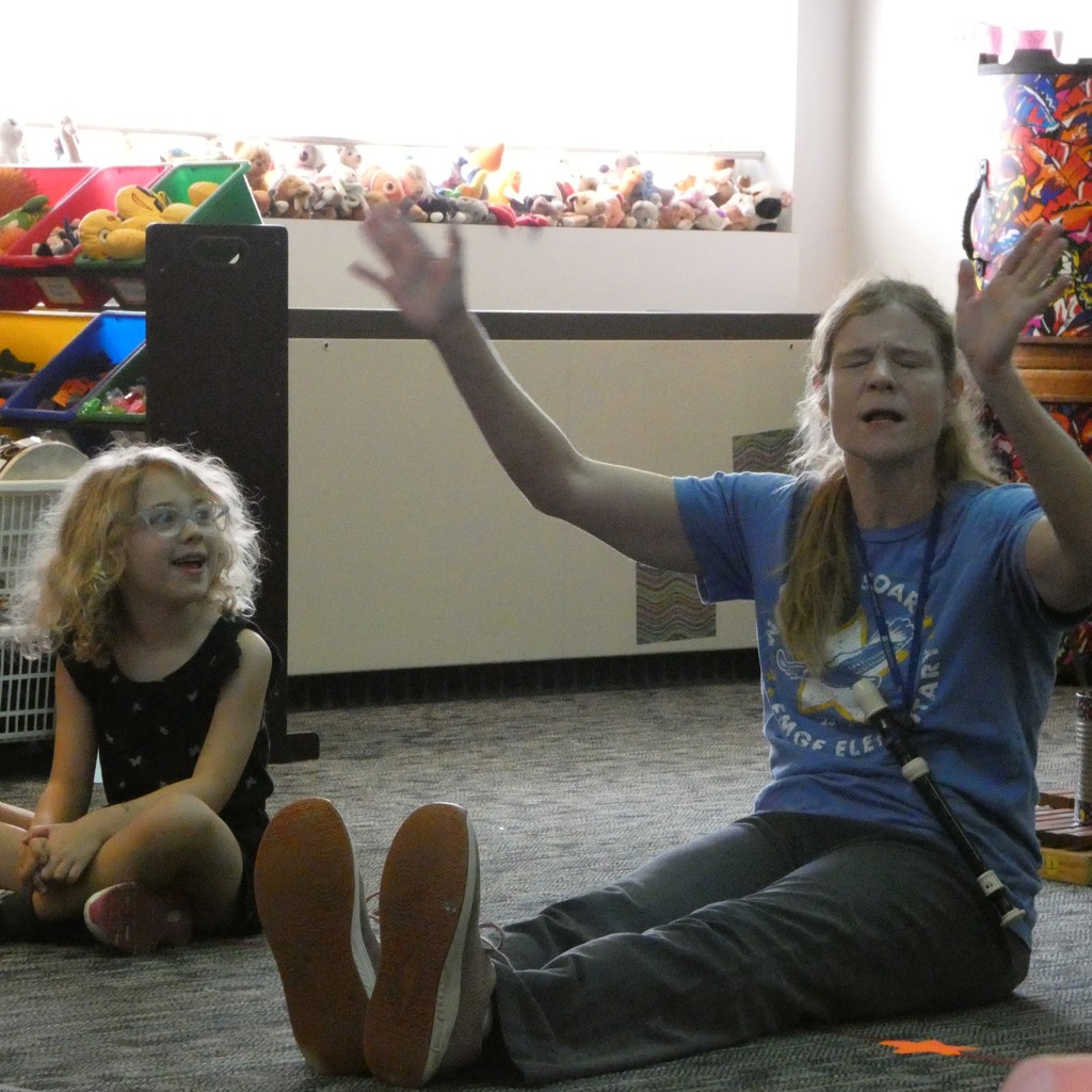 Music teacher closes her eyes and reaches to remember student's name while the student watches and laughs