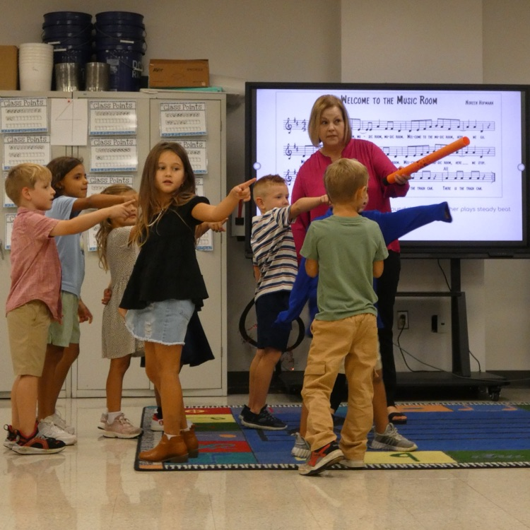 In front of big screen TV with the music to "Welcome to the Music Room" students point toward the Kleenex and the teacher points with boom-whackers
