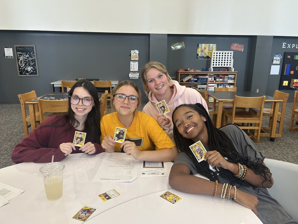 Four students at a table in library holding old Leader League trading cards.