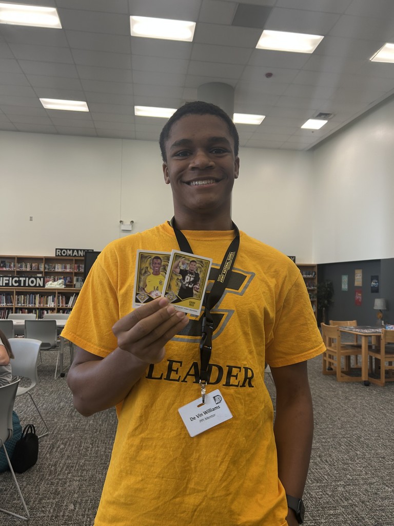 One student standing in library holding last year's Leader League trading cards.
