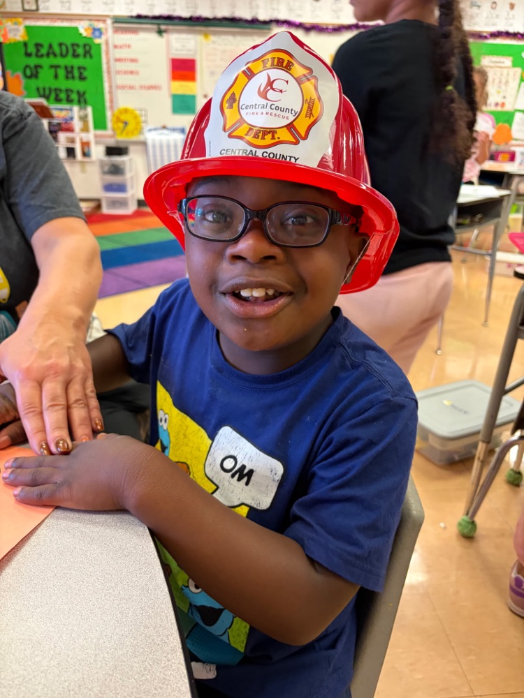 a second grader smiling so big wearing a central county fire hat