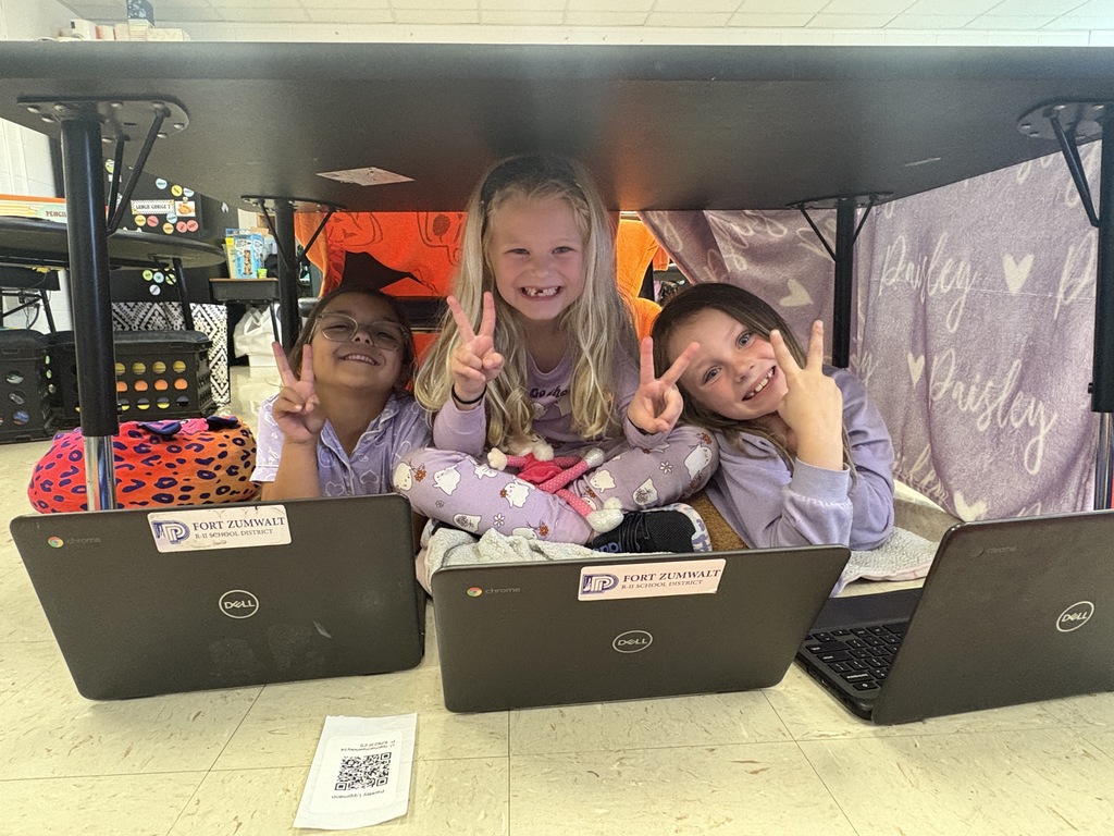 Three first-grade students working on their Chromebooks under their desk fort