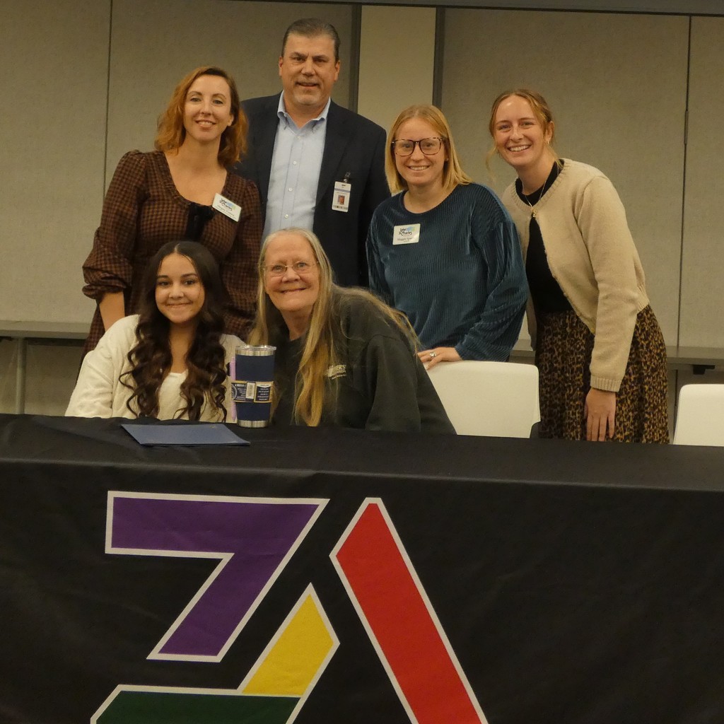 Proud family member jumps behind signing table for picture with student apprentice and employers