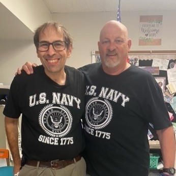 Arm-in-arm wearing their US Navy birthday shirts, veterans smile after leading students in the Pledge of Allegiance