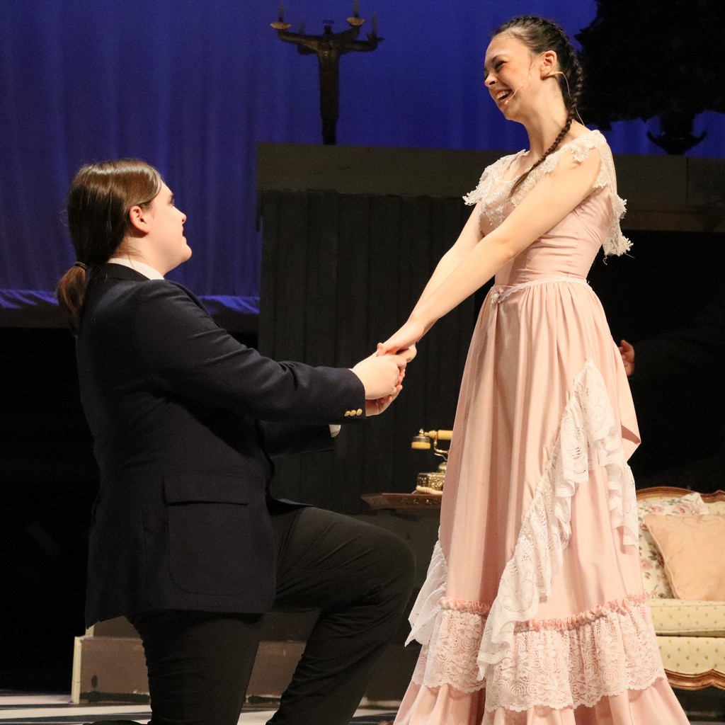 Student actors perform a scene, one on bended knee holds hands with other like a wedding proposal