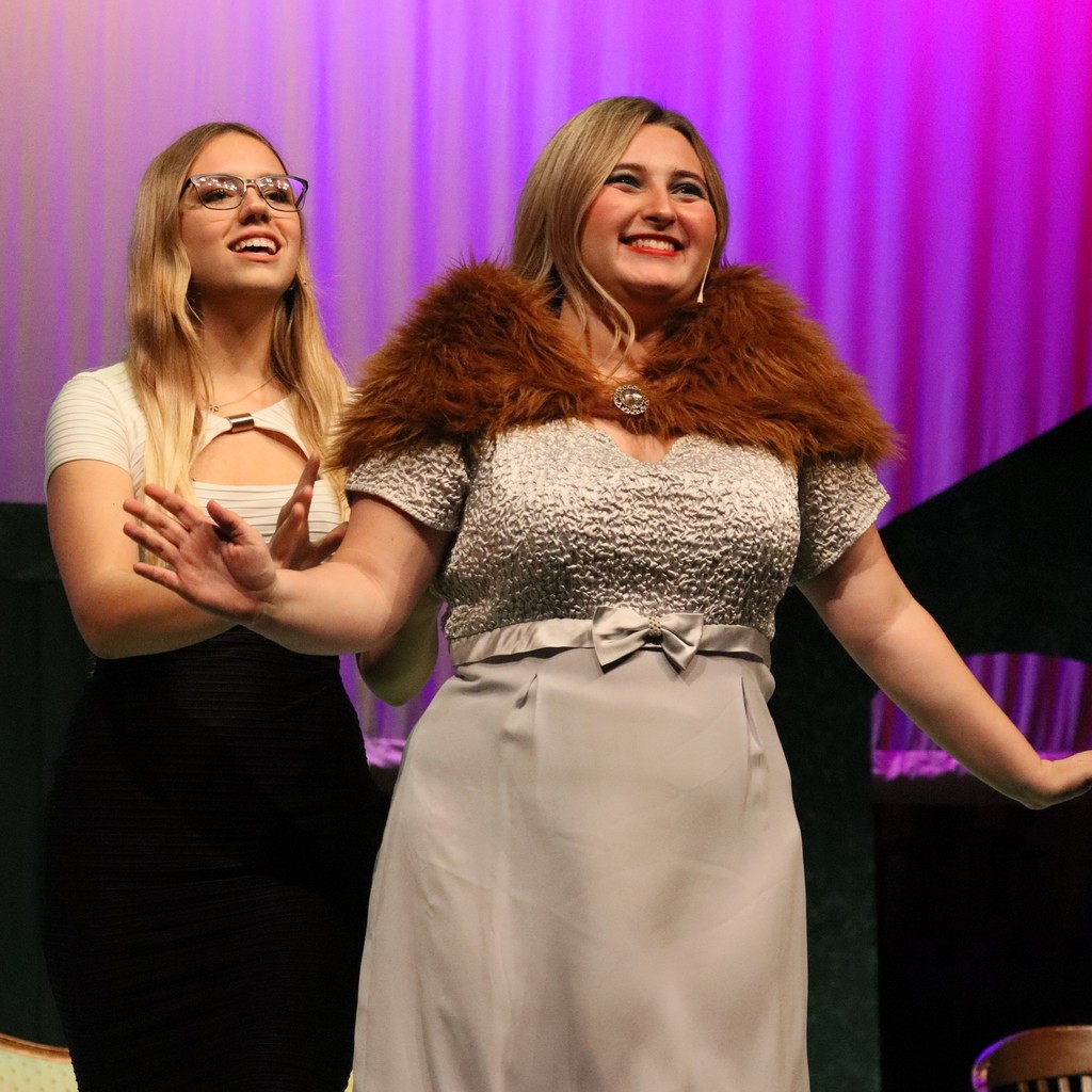 Student actors in evening gown costumes perform a scene