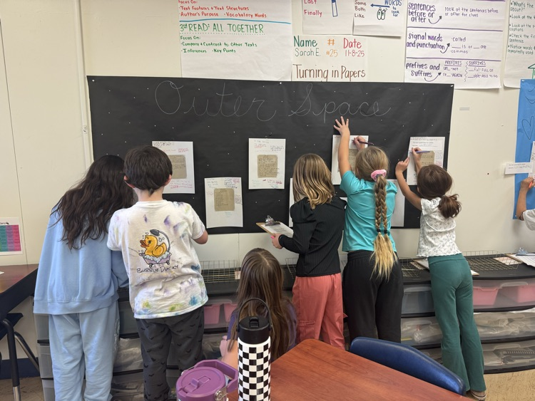 Students standing while writing feedback for each other at the end of their poetry unit 