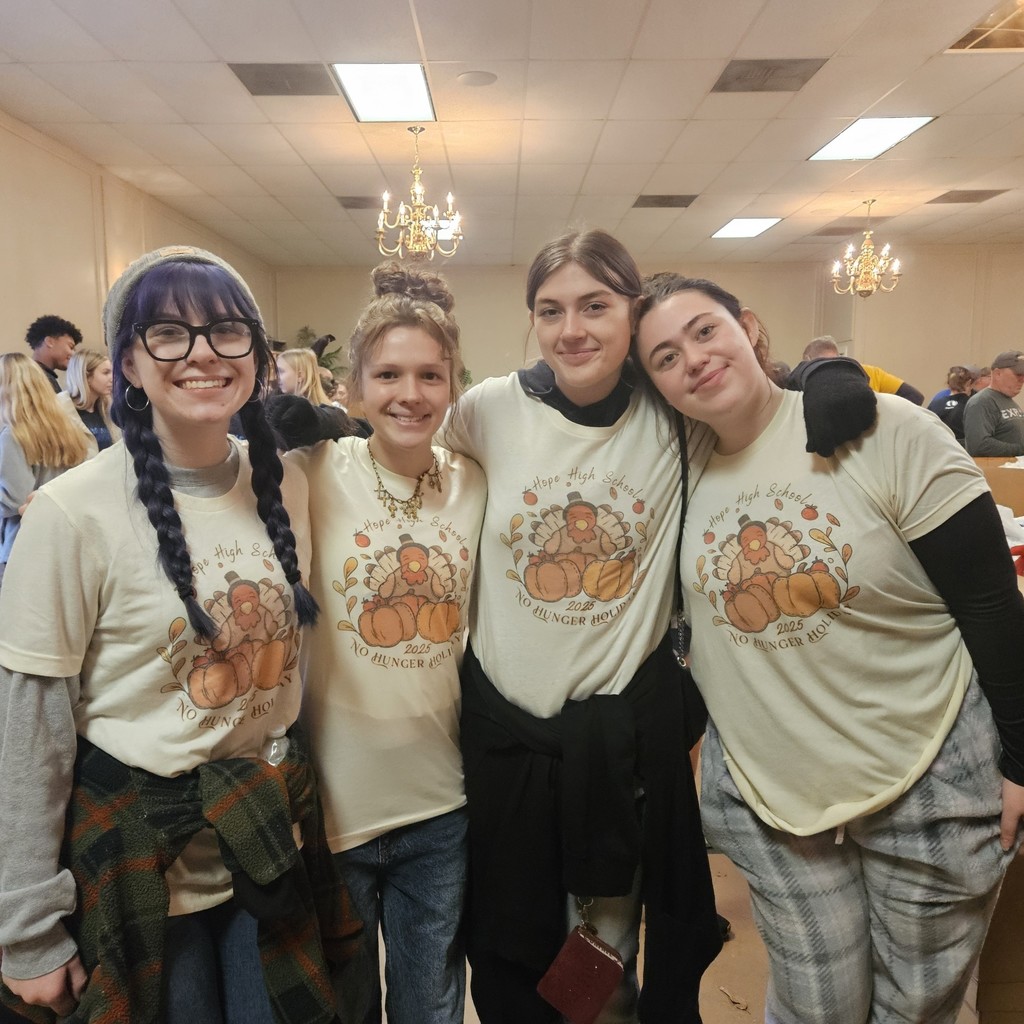 Students in matching thanksgiving shirts pause from packing meals for a picture