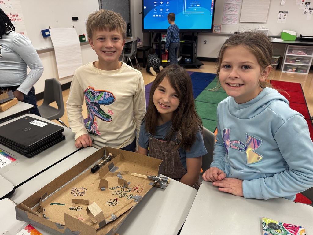 Three third graders posing in front of their pin ball machine, smiling with pride!